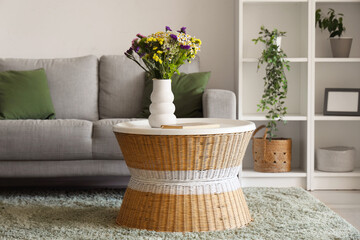 Cozy sofa and vase with wild flowers on coffee table in living room