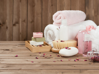 Spa Essentials on Wooden Table This image captures a serene spa setting with a variety of bath and body products neatly arranged on a wooden table. The composition includes rolled white and pink towel