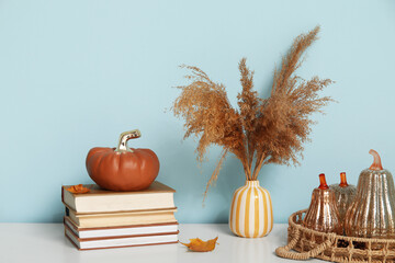Vase with pampas grass, decorative pumpkins, autumn leaves and books on shelf near blue wall