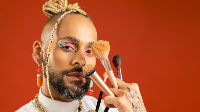 Homosexual man wear bright eyeshadow make up with makeup brush. LGBT community with freedom for homosexuals. Black gay applying make up looking camera