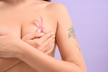 Fototapeta premium Naked young woman with pink ribbon on lilac background, closeup. Breast cancer awareness concept