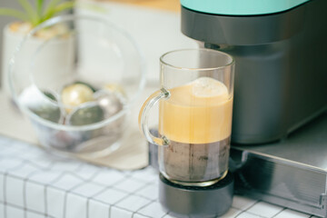 Close up coffee machine with capsules preparing americano in transparent glass at domestic kitchen at home. Espresso caffeine beverage maker and creamy italian drink