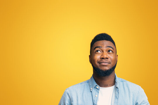 You must be kidding me. Cynical african american guy looking upwards at copy space on yellow studio background, panorama