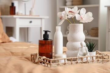 Vase with flowers and cosmetic products on bed in room, closeup