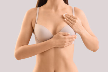 Young woman in bra on light background, closeup. Breast cancer awareness concept