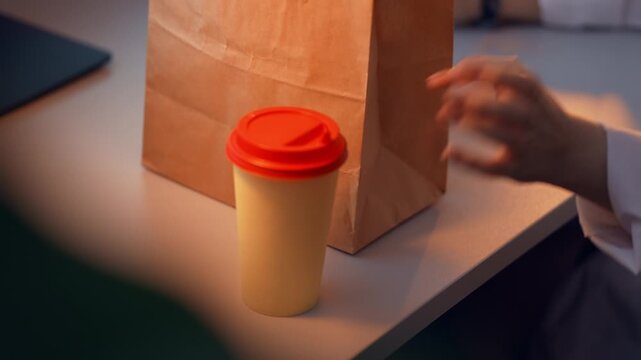 Woman in lab coat is sitting at the desk in front of computer and taking disposable cup of coffee filmed in slow motion. Young adult caucasian lady has hot drink during job in scientific laboratory