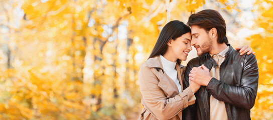Man and woman in love with closed eyes touching each other while having date at golden forest