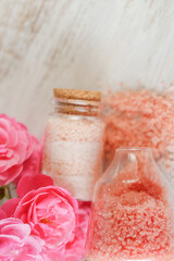  Rose salt with rose extract and fragrance.aromatic pink salt. Set of spa bath salts in glass jars and pink roses flowers on shabby white background.Aromatherapy and cosmetic.