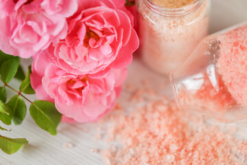 aromatic pink salt. Set of bath salts in glass jars and pink roses flowers on shabby white background. Rose salt with rose extract and fragrance. Aromatherapy and cosmetic.Organic cosmetics salt