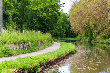 A scenic curved pathway along the Canal du Loing, surrounded by lush greenery and tranquil waters, offering a peaceful and picturesque setting