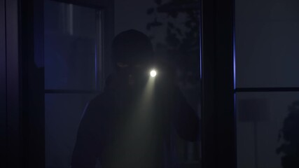 robbery, male thief in balaclava with flashlight in hands inspects the premises in search of valuables at night
