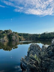 Calm water reflecting the blue sky and surrounding landscape, with rocks in the foreground. Ideal for nature and tranquility themes.