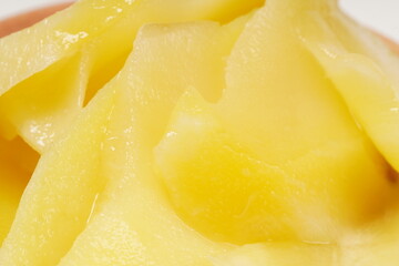 Young mango kickshaw, made from thinly sliced tangy yellow mango, placed on a wooden dish, photographed with a white background.