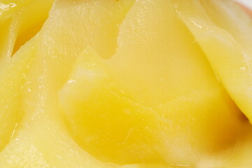 Young mango kickshaw, made from thinly sliced tangy yellow mango, placed on a wooden dish, photographed with a white background.