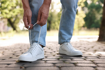 Man tying shoelace of white sneaker outdoors, closeup