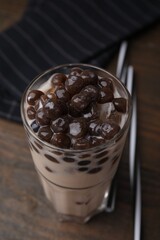 Tasty milk bubble tea in glass on wooden table, closeup