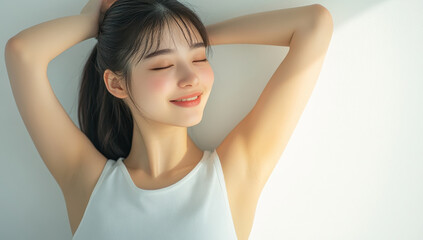 an Asian woman in a tank top with arms raised, emphasizing her natural beauty and relaxed style against a gentle, soft-lit backdrop.