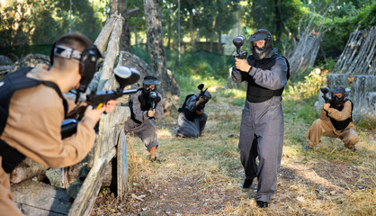 Fototapeta premium Team eliminating opponents on paintball field. People in protective outwear and helmets aiming with paintball markers.