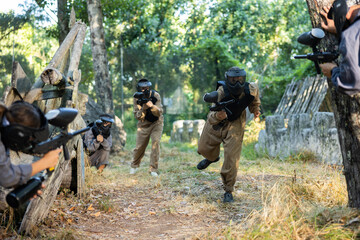 Group of men and women in protective clothes and helmets shooting with paintball markers. Teams...