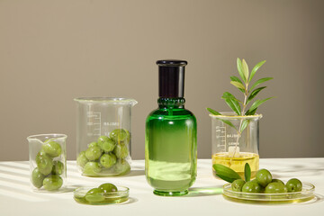 In the center is an unlabeled green glass jar, next to it are olive ingredients placed in glass laboratory equipment. The natural theme for vegan cosmetic