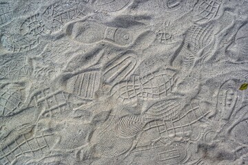 A dense network of various shoe prints and footprints covers a light-colored sand or dirt surface,...