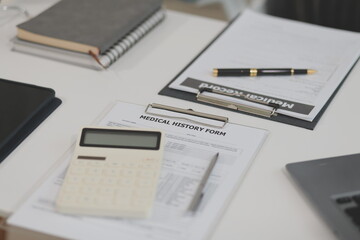 Doctor's working on laptop computer, writing prescription clipboard with record information paper folders on desk in hospital or clinic, Healthcare and medical concept. Focus on stethoscope