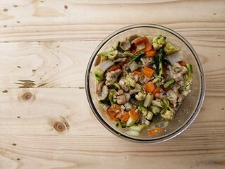 A vibrant mix of cooked vegetables and protein fills a clear glass bowl, placed on a warm wooden surface with ample copy space