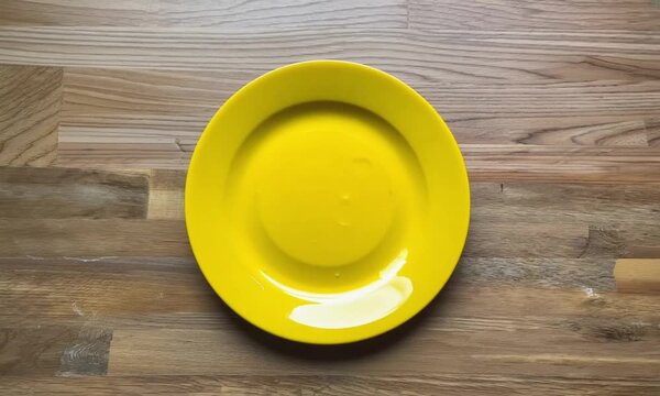 woman hand placing empty yellow plate on wooden table