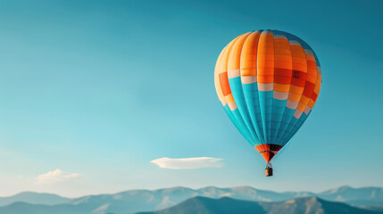 Obraz premium A colorful hot air balloon floating in a clear blue sky with distant mountains, representing adventure, freedom, and travel.