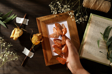 Dried flowers and plants, photo frame, book and hand on wooden background, top view