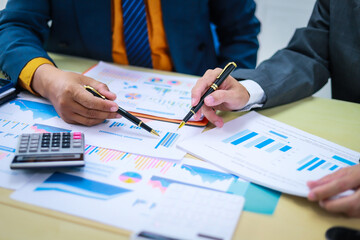 Two businessmen are seated at a desk in an office, engaged in a meeting focused on analysis, finance, and marketing strategies, with documents and graphs spread across the table.