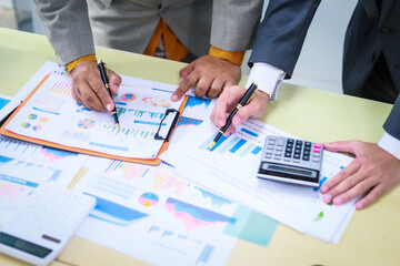 Two businessmen are seated at a desk in an office, engaged in a meeting focused on analysis, finance, and marketing strategies, with documents and graphs spread across the table.