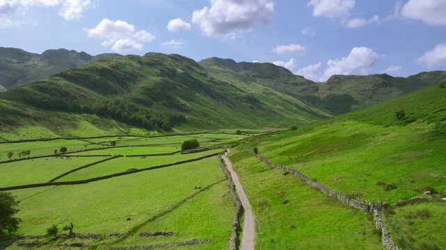 Flying over and along valley path with surrounding mountains. Mickleden, The Langdales, Lake District, UK