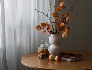 A cozy still life on a wooden table - a jar of oatmeal cookies, apples, an autumn bouquet, notebooks. Cozy autumn house