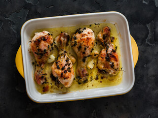 Baked chicken legs with thyme, garlic and paprika in a baking dish on a dark background
