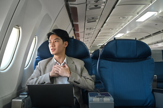 Young businessman looking out the window with hand resting on his chest, experiencing aerophobia or fear of flying