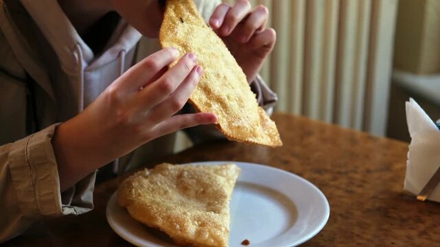 A young girl eats a fried cheburek pie sitting at a table in a cafe.
