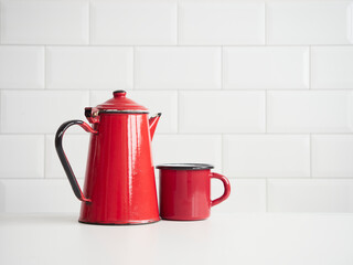 old fashion red enameled steel coffee pot and mug on table with white tile backgrounds and copy space. Concept of kitchen utensils and coffee