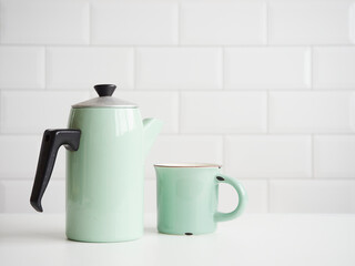 old fashion light green enameled steel coffee pot and mug on table with white tile backgrounds and copy space. Concept of vintage kitchen utensils and coffee