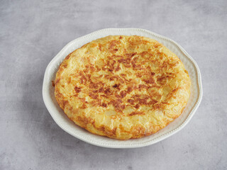 high angle view of tasty Spanish potato omelet served whole on a plate on a grey countertop