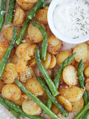 close up full frame view of roasted potatoes with green asparagus with yogurt bowl sauce and sea salt