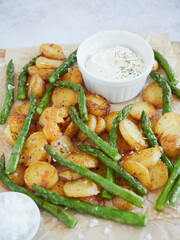 close up view of roasted potatoes with green asparagus served on paper with yogurt bowl sauce and sea salt for seasoning