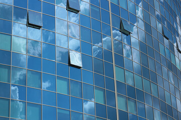 Blue sky is reflected in the windows of a multi-story office building. Abstract city background.