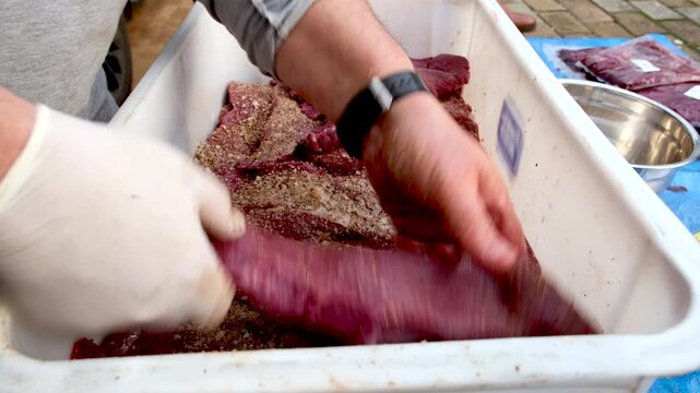 Venison steak strips spiced and stacked for curing in container, biltong making