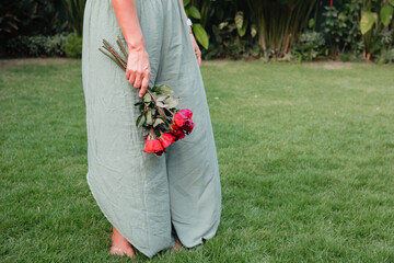 Woman in green boho pants holding red roses in the garden. The concept of a date and congratulations on Valentine's Day. Bouquet of flowers for a holiday and wedding © Anastasia Studio