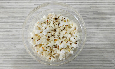 popcorn closeup with a delicious salty taste placed in a clear glass bowl as a snack for watching a movie, or relaxing watching TV, relaxing with family isolated on a white wooden texture background