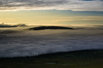 Fjätervålen mountain peak emerges from a sea of fog, bathed in warm golden sunlight, as the morning mist rolls over the valley landscape in Särna Dalarna, Sweden © Dylan