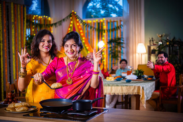 Indian old woman and young daughter in traditional cloths cooking food for Diwali festival at home