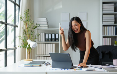 Asian businesswoman laughing happily at work happy looking at the laptop screen Excited about online victories. Watch funny videos on your computer. Enjoy good news on the internet.