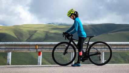 Fototapeta premium Cyclist with road bike on grassland mountain top trail